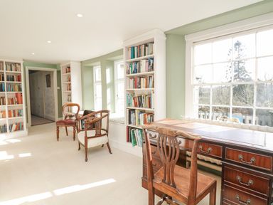 A room with bookshelves chairs a wooden desk and windows with green walls at Wootton House in Butleigh Wootton near Compton Dundon