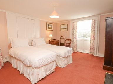 A bedroom with two single beds a wooden chest of drawers two chairs a window with floral curtains and carpet flooring at Wootton House in Butleigh Wootton near Compton Dundon