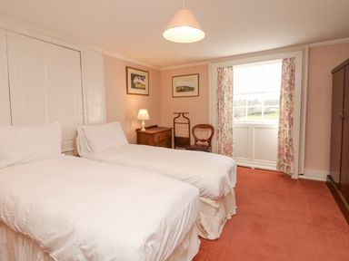 A bedroom with two single beds white bedding a wooden chest of drawers a chair floral curtains and a window at Wootton House in Butleigh Wootton near Compton Dundon