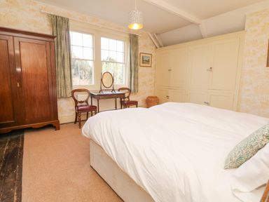 A bedroom with a double bed white bedspread wooden wardrobe dressing table and chairs at Wootton House in Butleigh Wootton near Compton Dundon