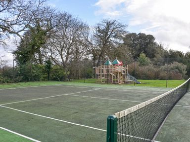 An outdoor tennis court with a playground area and trees in the background at Wootton House in Butleigh Wootton near Compton Dundon