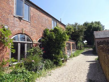 A brick house with arched windows and plants along a gravel path at Pittards Farm Cottage in South Petherton