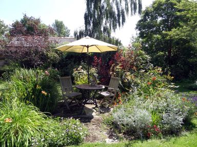 A garden with a round table and two chairs under a yellow umbrella surrounded by plants at Pittards Farm Cottage in South Petherton