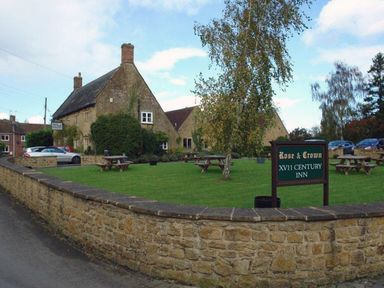 An outdoor area with picnic tables and a sign for Rose and Crown XVII century inn near a stone building at Pittards Farm Cottage in South Petherton