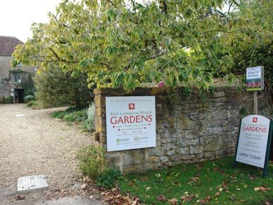 Stone wall and signs for East Lambrook Manor Gardens with a gravel path and plants at East Lambrook Manor Gardens in South Petherton