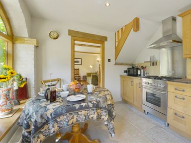 A kitchen with a table set for two and wooden cabinets at Pittards Farm Cottage in South Petherton