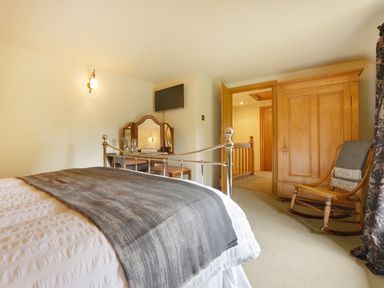 A bedroom with a metal bed frame a wooden wardrobe a rocking chair and a dressing table at Pittards Farm Cottage in South Petherton