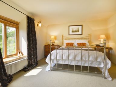 A bedroom with a metal bed frame two bedside tables with lamps a window with curtains and boots on the sill at Pittards Farm Cottage in South Petherton