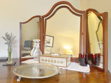 A wooden dressing table with a three-panel mirror crystal decanters a decorative box red glasses and a vase with flowers at Pittards Farm Cottage in South Petherton