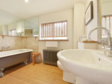 A bathroom with a clawfoot bathtub a wooden stool a radiator a window with blinds and a sink with a mirror at Pittards Farm Cottage in South Petherton