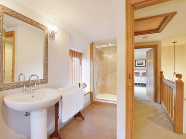 A bathroom with a pedestal sink mirror and shower visible beyond a doorway at Pittards Farm Cottage in South Petherton