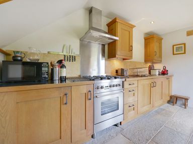 A kitchen with wooden cabinets a gas stove a microwave a kettle and kitchen utensils at Pittards Farm Cottage in South Petherton