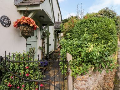 A stone pathway leading to a mint green door with a hanging basket and garden gate at Castle View in Dunster
