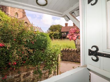 View through an open window showing bushes a stone wall and buildings outside at Castle View in Dunster
