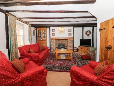 A living room with red upholstered seating a wooden coffee table a fireplace and a television at Castle View in Dunster