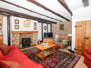A living room with a red sofa a wooden coffee table a tv on a chest of drawers and stone walls at Castle View in Dunster