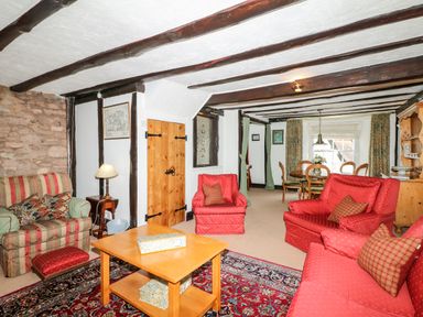 A living room with red armchairs a striped armchair a wooden coffee table and dining table at Castle View in Dunster