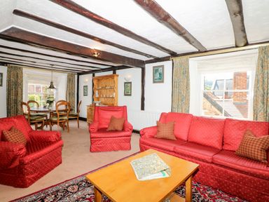 A living room with red sofas a wooden coffee table and a dining table with chairs at Castle View in Dunster