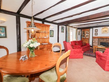 A room with wooden dining table and chairs a wooden cabinet red sofas a coffee table and a fireplace at Castle View in Dunster