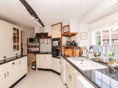 A kitchen with white cabinets black countertops a sink a window with striped curtains and various kitchen utensils at Castle View in Dunster