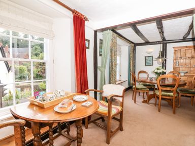 A dining area with two wooden tables and chairs near windows with curtains at Castle View in Dunster