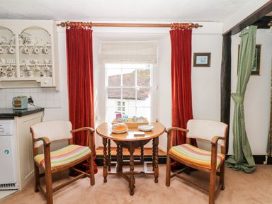 A dining area with a wooden table and two chairs with striped cushions in front of a window with red curtains at Castle View in Dunster