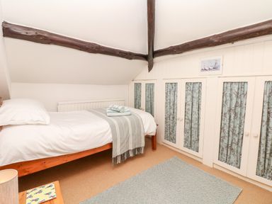 A bedroom with a single bed wooden beams on the ceiling and built in cupboards with patterned curtains at Castle View in Dunster