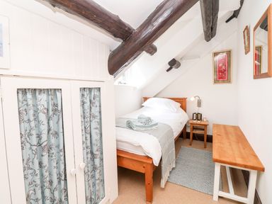 A small bedroom with a single bed wooden bench and wardrobe with patterned curtains at Castle View in Dunster