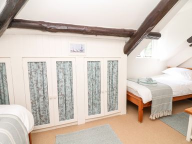 A bedroom with two single beds two rugs and built in white cupboards with blue patterned curtains at Castle View in Dunster