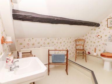 A bathroom with a sink, towel rack, wooden chair, and toilet under a sloped ceiling with a wooden beam at Castle View in Dunster