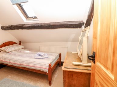 A small bedroom with a single bed striped bedding a wooden dresser with a mirror and a skylight window at Castle View in Dunster