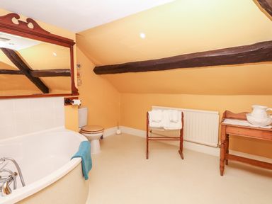 A bathroom with a bathtub a toilet a wooden towel rack with towels and a wooden table with a ceramic pitcher at Castle View in Dunster