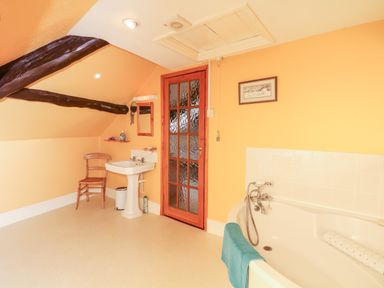 A bathroom with a corner bathtub a pedestal sink a wooden chair and a wooden door at Castle View in Dunster