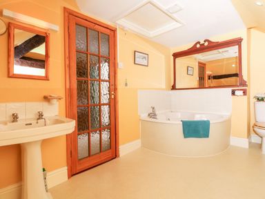 A bathroom with a pedestal sink wooden framed mirror a corner bathtub with a towel and a toilet at Castle View in Dunster