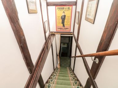 A staircase with green carpet and wooden handrail leading down with framed pictures on white walls at Castle View in Dunster
