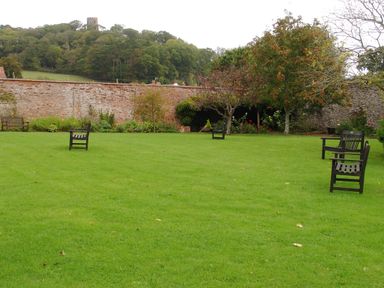 A garden with green lawn and wooden benches near trees and a brick wall at Castle View in Dunster