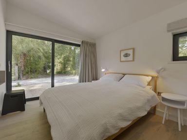 A bedroom with a double bed next to a sliding glass door and a small round white side table at Grooms Cottage in Talaton near Ottery St Mary