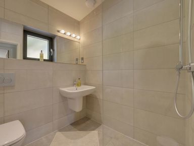 A bathroom with a wall-mounted sink toilet shower and a window at Grooms Cottage in Talaton near Ottery St Mary