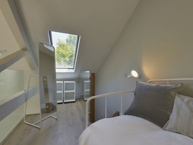 A loft bedroom with a white metal bed frame pillows a standing mirror two white shelves and a skylight window at Grooms Cottage Talaton near Ottery St Mary