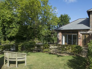 A garden with a wooden bench and hedges next to a brick building with a slate roof at Grooms Cottage in Talaton near Ottery St Mary