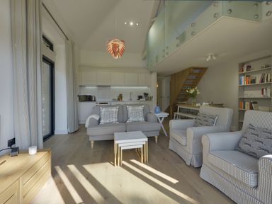 A living room with sofa armchairs and coffee tables with kitchen dining area and wooden staircase at Grooms Cottage Talaton near Ottery St Mary