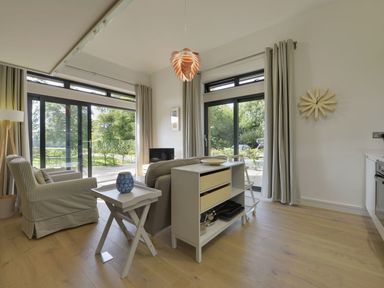A living area with armchairs a small table and storage unit near sliding glass doors at Grooms Cottage Talaton near Ottery St Mary