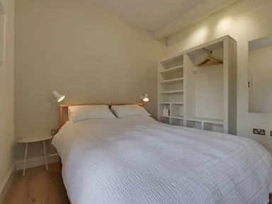 A bedroom with a double bed white bedding bedside table and wall shelves with hangers at Gardeners Cottage in Talaton near Ottery St Mary