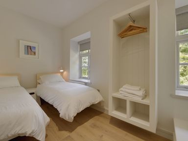 A bedroom with two single beds a window an open closet with hangers and folded towels at Gardeners Cottage in Talaton near Ottery St Mary