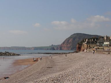 A pebble beach with people near the water and houses on cliffs in the background at Gardeners Cottage in Talaton near Ottery St Mary