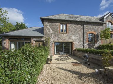 An outdoor patio area with a table and chairs a charcoal grill hedges and a stone house wall at Gardeners Cottage in Talaton near Ottery St Mary
