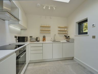 A modern kitchen with white cabinets countertop and appliances including oven kettle toaster and microwave at Gardeners Cottage in Talaton near Ottery St Mary