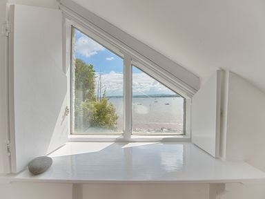 A triangular window with white shutters open showing a view of water trees and boats at 1 The Quay in Lympstone