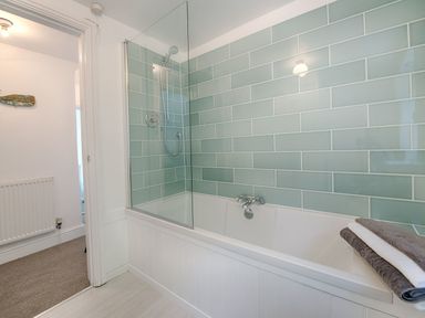 A bathroom with a bathtub shower combination and folded towels on the tub at 1 The Quay in Lympstone
