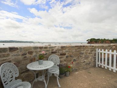 A stone patio with metal table and chairs and flower pots overlooking a body of water with boats at 1 The Quay in Lympstone